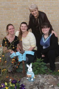 (Pictured L-R) UIW students Kaime Roe, Kerri Rodriguez, and Megan Wellington, share a photo with Dr. Mary Ruth Moore (standing) with the Peter Rabbit statue in the  garden.  The small jacket was handmade by Wellington.