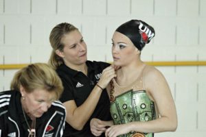 Gerdin (center) assists Cardinal Madison Delgado with her suit at a synchronized swimming competition. 